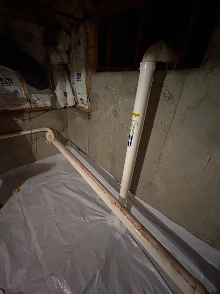 Radon suction point rising from the slab beside a freshly laid vapour barrier and wall insulation