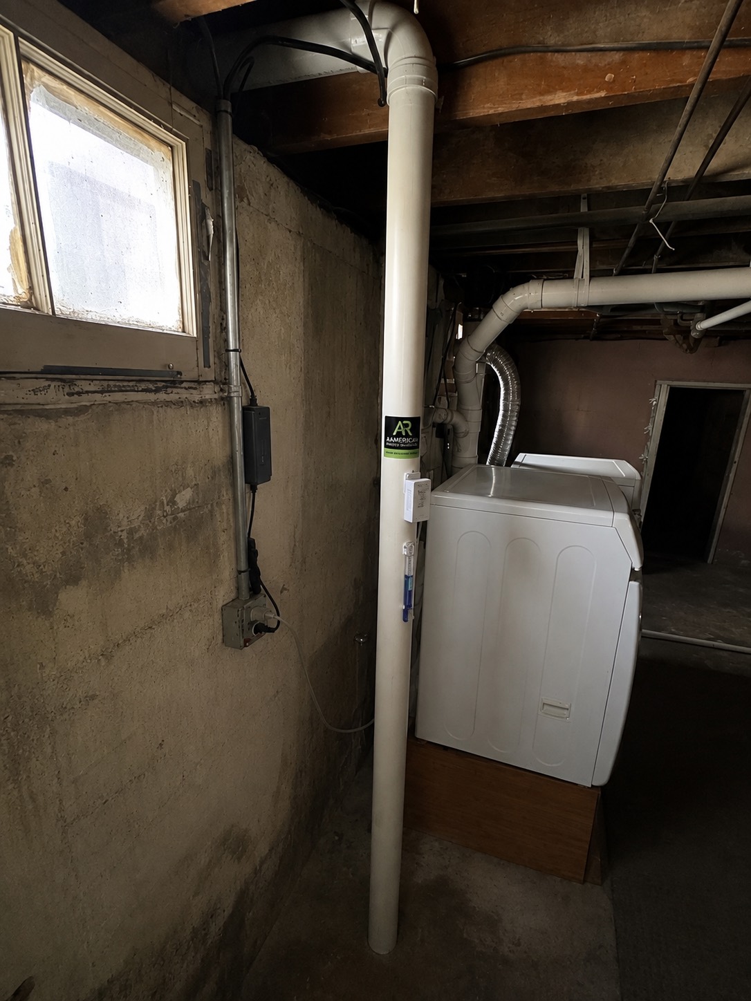 Radon mitigation pipe running floor to ceiling in a Colorado basement beside the laundry, with the system manometer visible